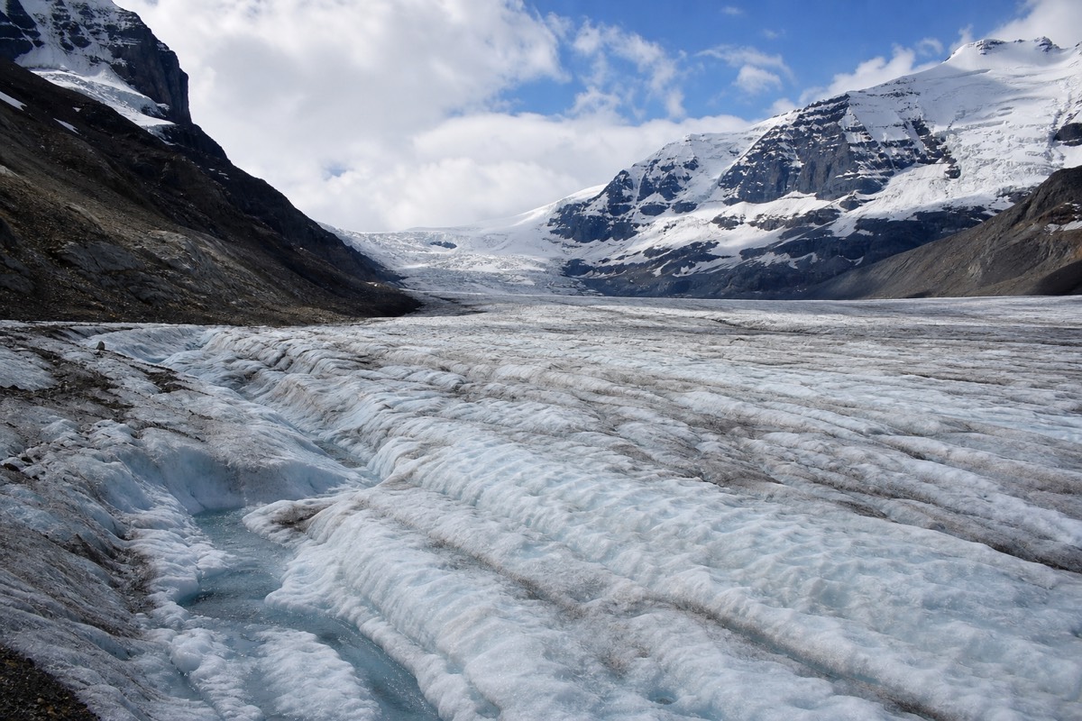 The rippled blue-white surface of the Athabasca Glacier flowing down between dark mountain ridges at the Columbia Icefield