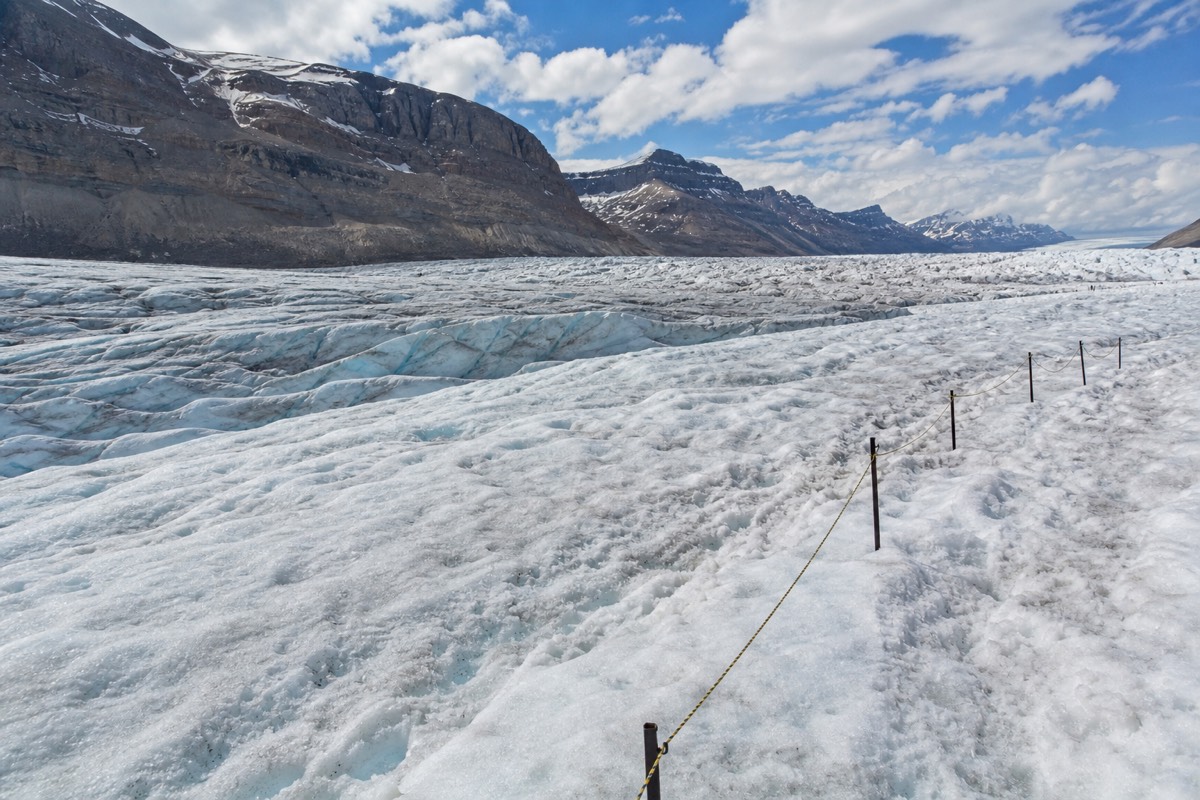 A small group in warm layers walking on the rippled blue-white surface of the Athabasca Glacier below the Columbia Icefield