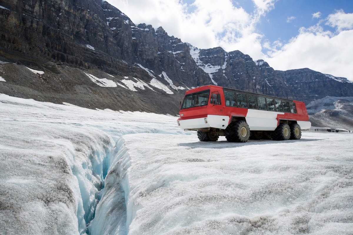 A massive red-and-white Ice Explorer all-terrain vehicle parked on the surface of the Athabasca Glacier with passengers walking on the ice