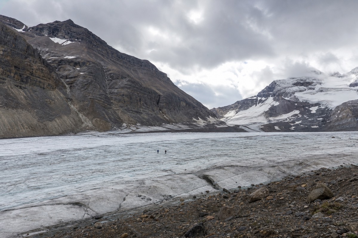 An Ice Explorer parked on the Athabasca Glacier with visitors walking on the ice below Rocky Mountain peaks